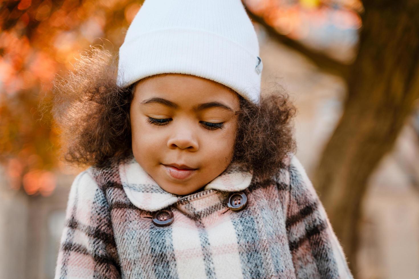 ragazza riccia nera che indossa un cappello bianco che cammina nel parco autunnale foto