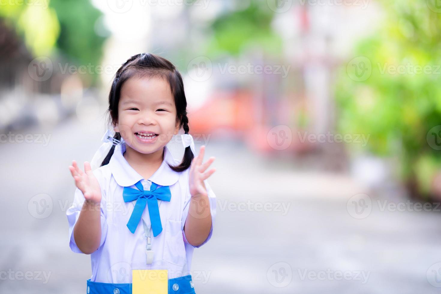 studenti dell'asilo che indossano l'uniforme scolastica blu e bianca, standing ovation, felici di andare a scuola. dolce sorriso la mattina del giorno di apertura del semestre. trecce a maglia bambino asiatico su entrambi i lati. di 3 anni foto