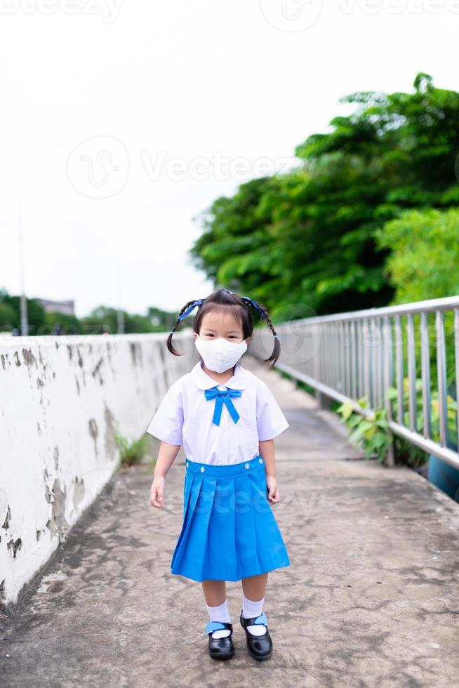 bambino che indossa uniformi scolastiche e maschere va a scuola. bambini che camminano per strada. i bambini sorridono dolcemente. ragazza dell'asilo con una nuova vita normale. prevenire la diffusione di virus e polveri tossiche. bambino 3-4 anni. foto