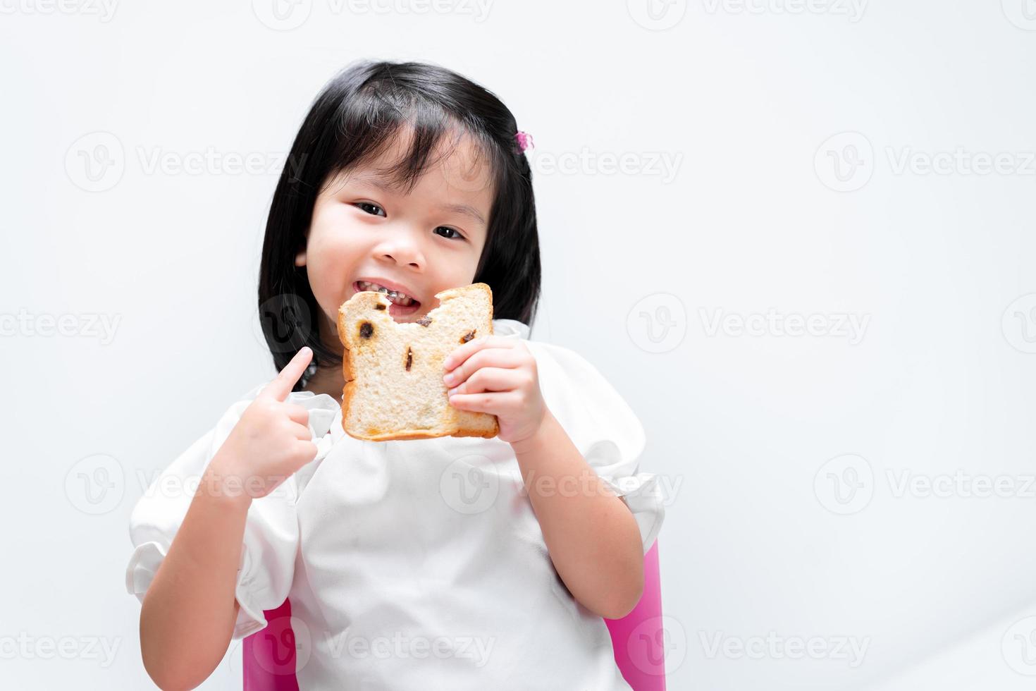 adorabile bambino che tiene le fette di pane all'uvetta. bambino che punta il dito indice sul cibo. sorriso dolce ragazza felice. i bambini si divertono a mangiare. su sfondo bianco. foto