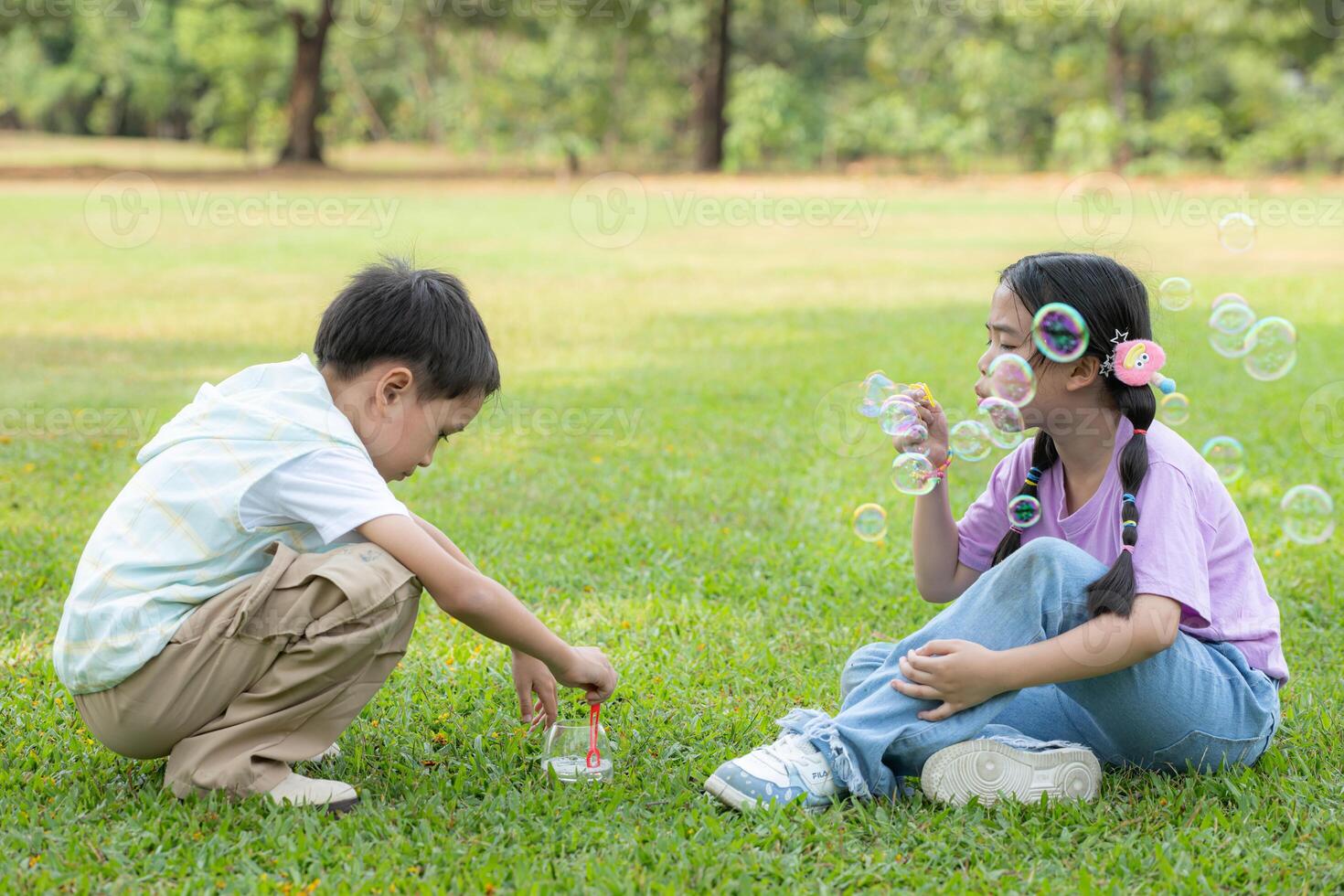 bambini seduta nel il parco con soffiaggio aria bolla, circondato di verdura e natura foto