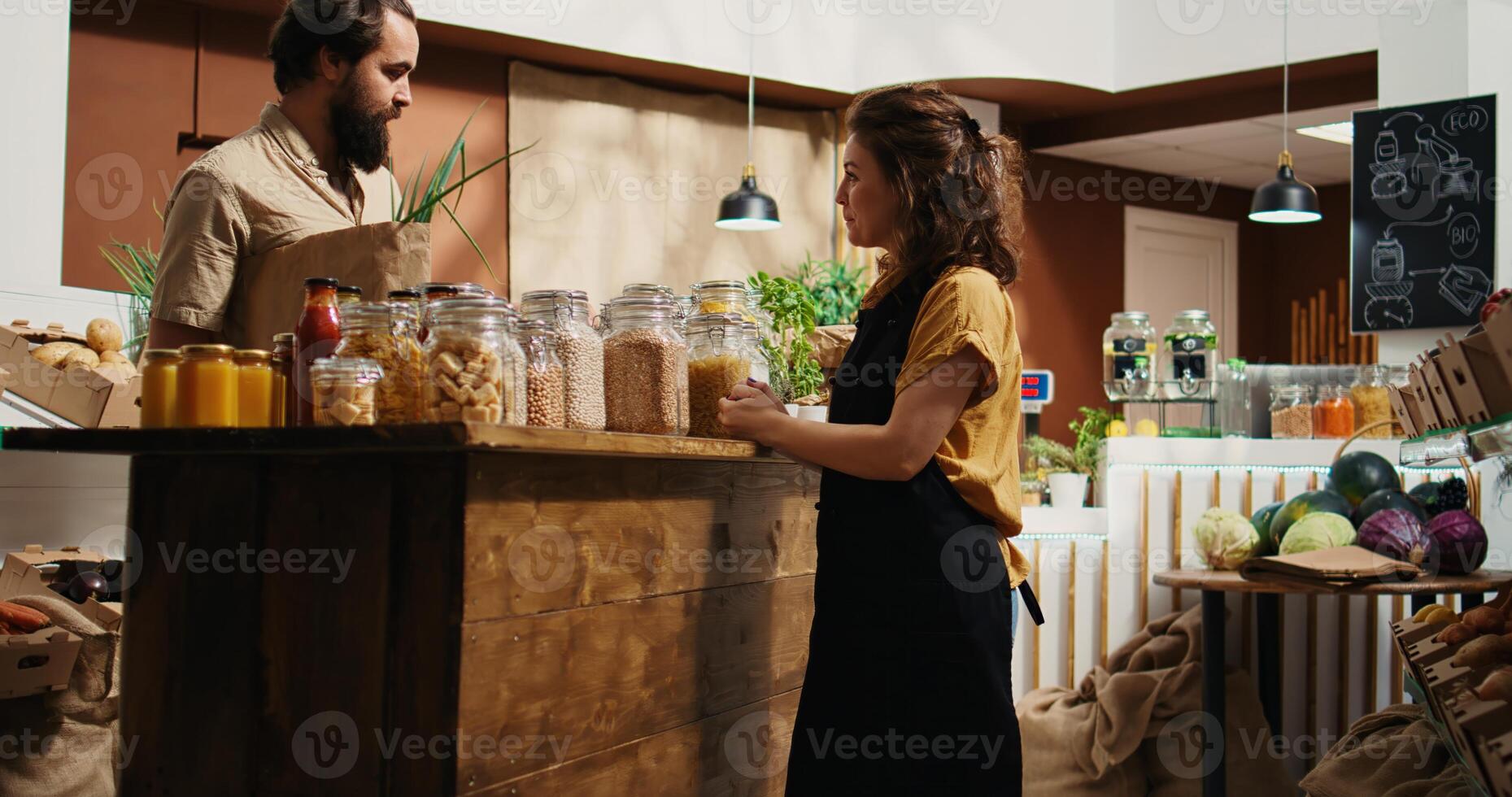 uomo nel zero rifiuto supermercato utilizzando carta Borsa per Acquista la verdura, ottenere Aiuto a partire dal amichevole venditore. donna Lavorando nel Locale Quartiere drogheria negozio assistere cliente con Informazioni foto