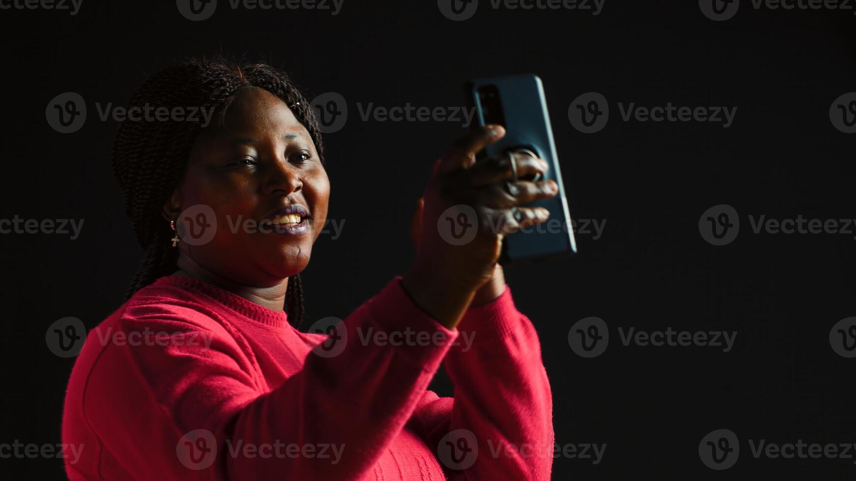 un' allegro donna nel nero sfondo agitando a un' video chiamata su sua smartphone avendo un' lontano interazione su un Internet video conferenza. discussione su mobile Telefono attraverso video conferenza. foto