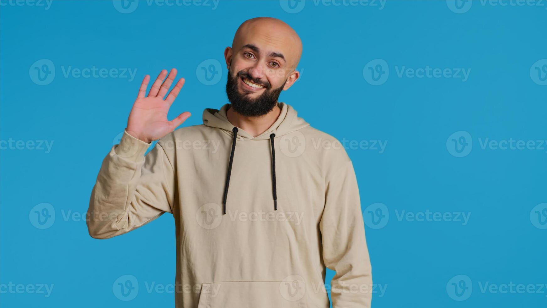 mezzo orientale tipo saluto persone nel davanti di telecamera, agitando Ciao e sorridente al di sopra di blu sfondo. giovane persona in posa con fiducia nel studio, sensazione fiducioso e gioioso. telecamera 1. foto