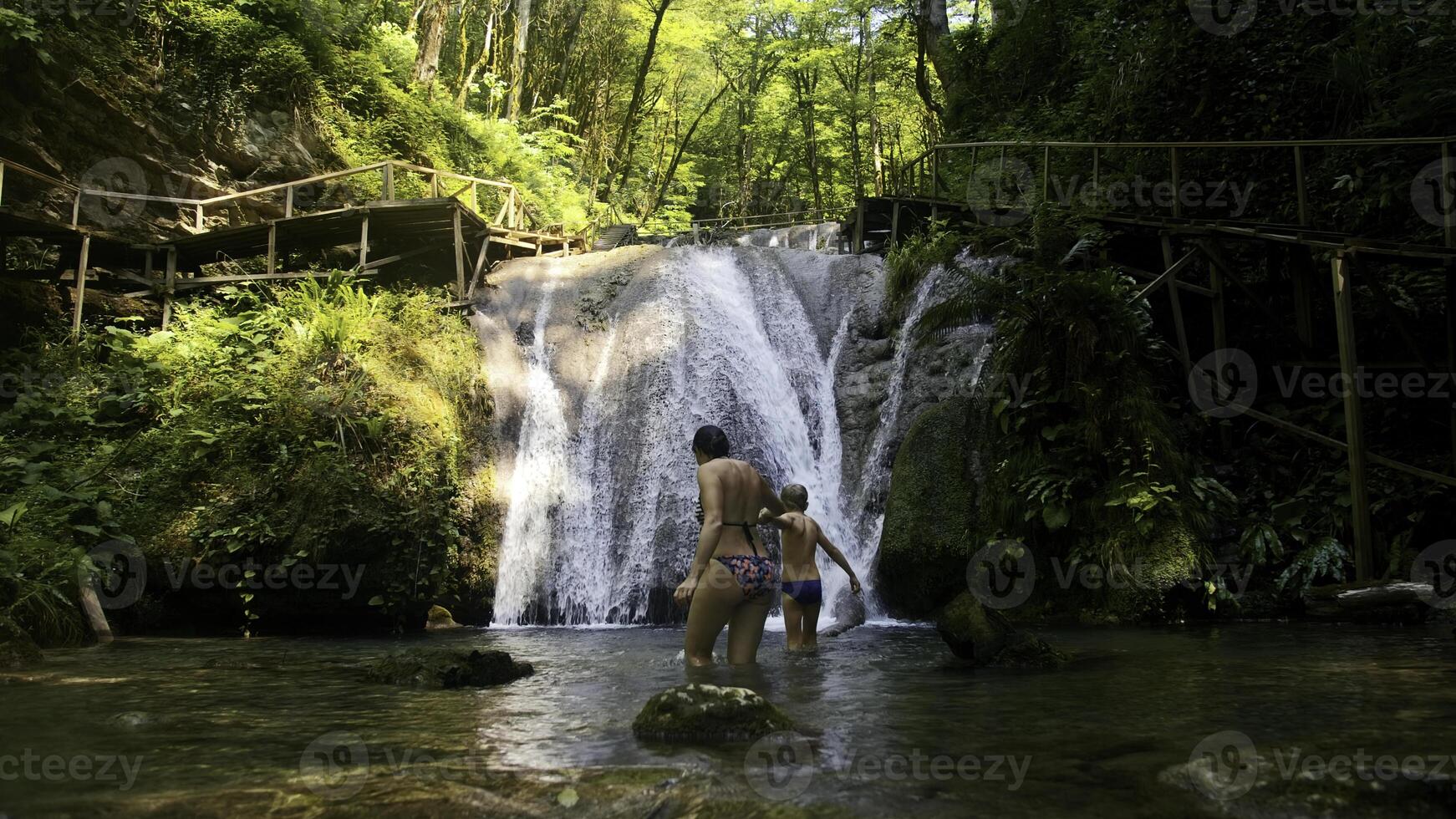 donna e ragazzo bambino bagnarsi nel bellissimo cascata nel denso giungle. creativo. donna e un' ragazzo nel freddo montagnoso fiume. foto