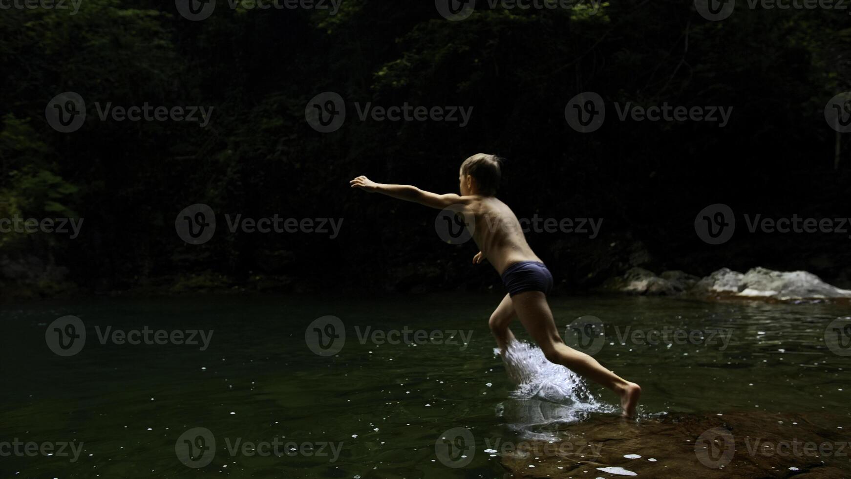 lento movimento di un' ragazzo salto in un' cascata e naturale stagno. creativo. giovane ragazzo bambino avendo divertimento nel giungle. foto