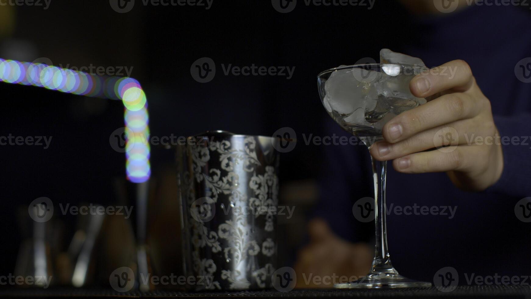 vicino su barista lancio lontano ghiaccio cubi a partire dal un' piccolo cocktail bicchiere. media. raffreddamento un' bicchiere per fabbricazione un' cocktail. foto