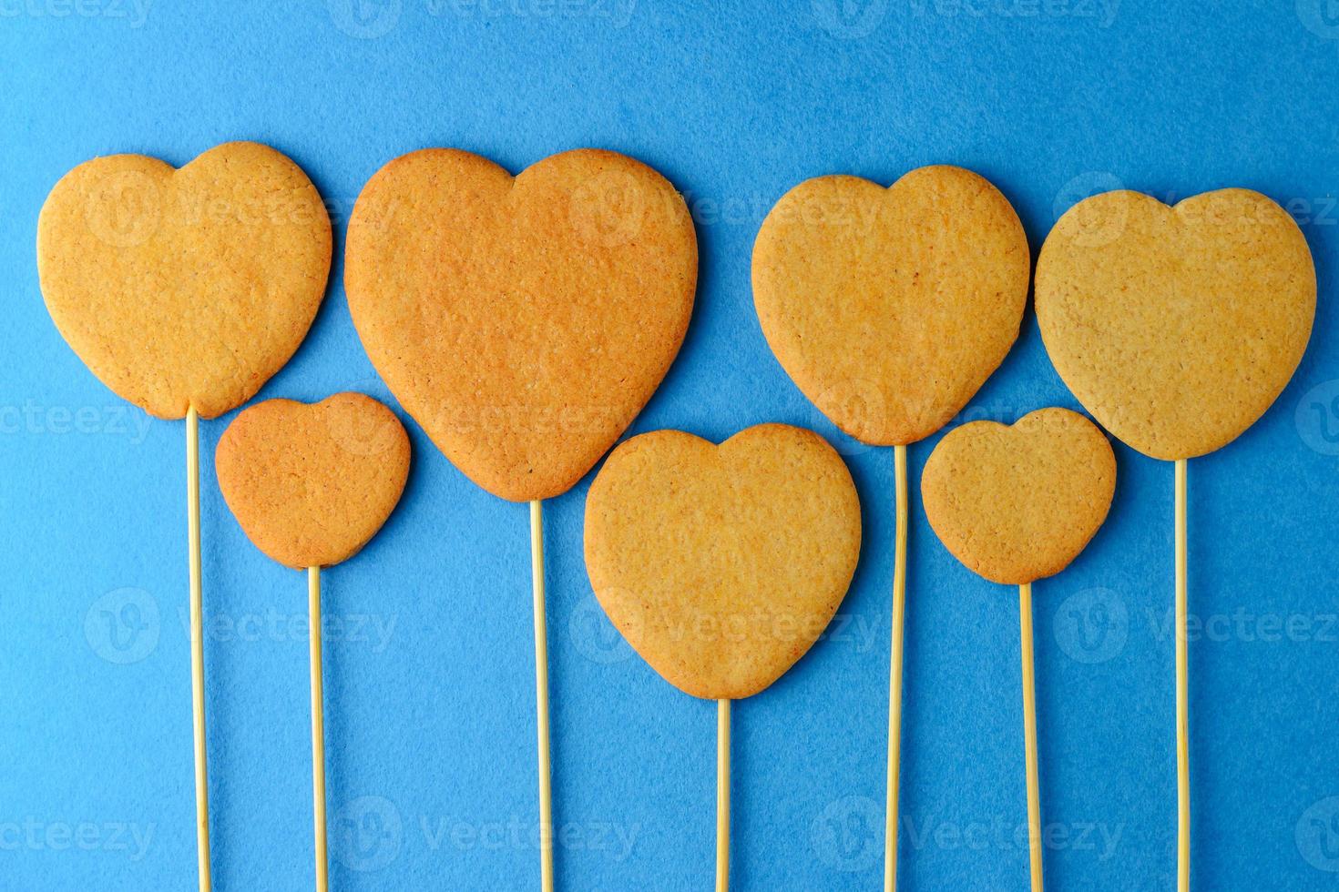 biscotti allo zenzero su un bastoncino a forma di cuore su sfondo blu foto