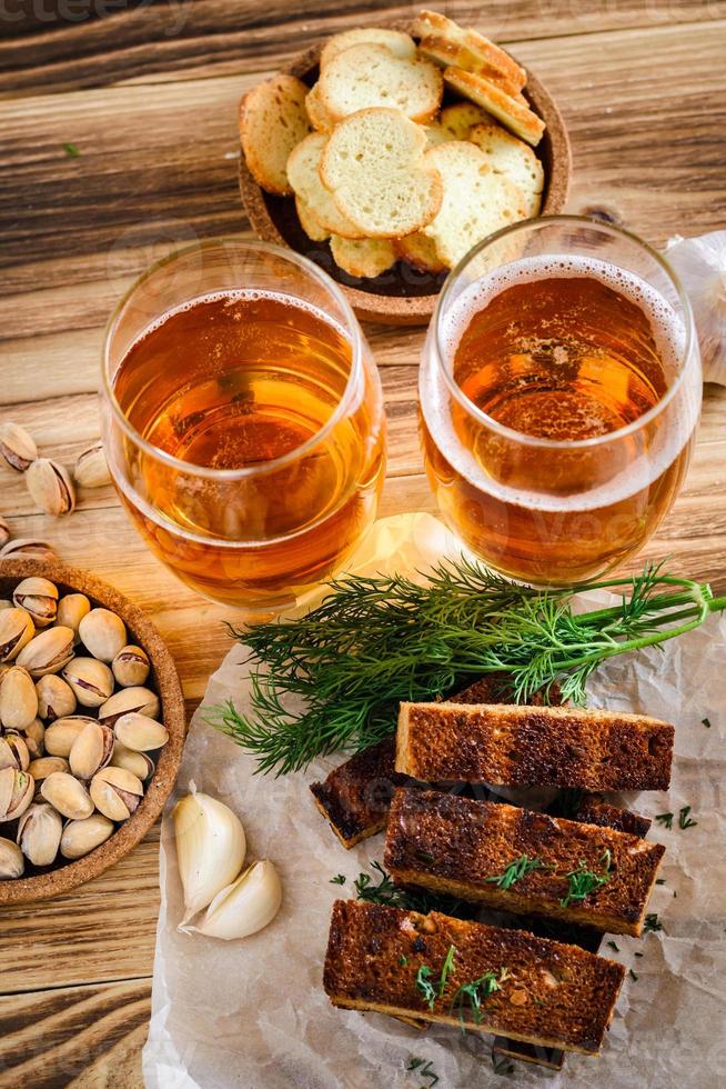 due bicchieri di birra chiara, pistacchi e crostini su un tavolo di legno. foto