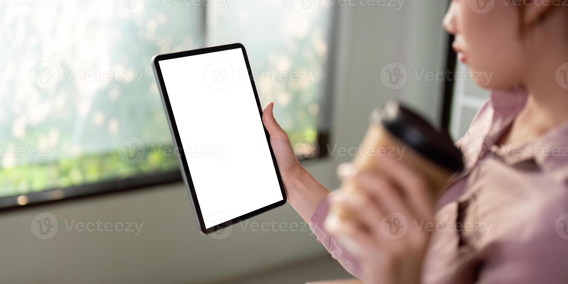 modello di un' donna Tenere digitale tavoletta con vuoto bianca del desktop schermo con Tenere un' caffè tazza foto
