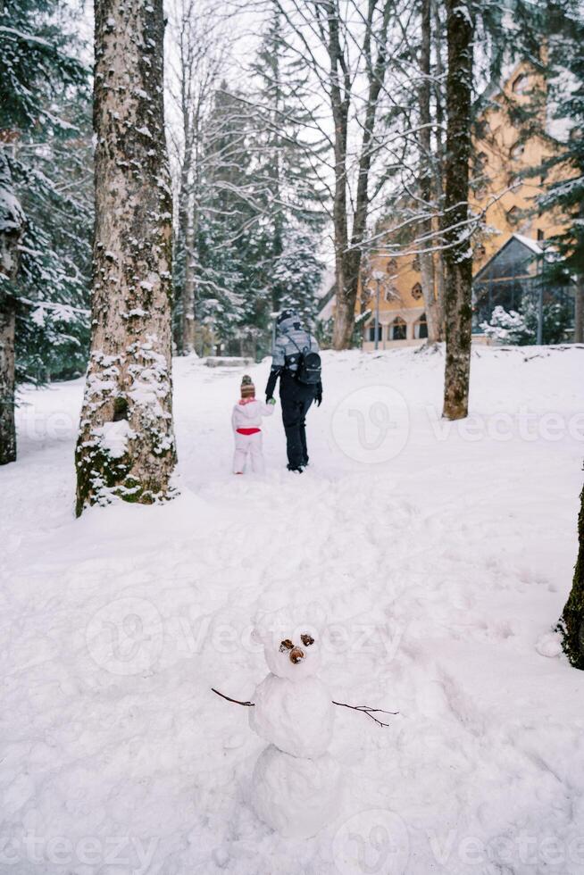pupazzo di neve sta nel un' nevoso foresta contro il fondale di un' in partenza madre con un' piccolo bambino foto