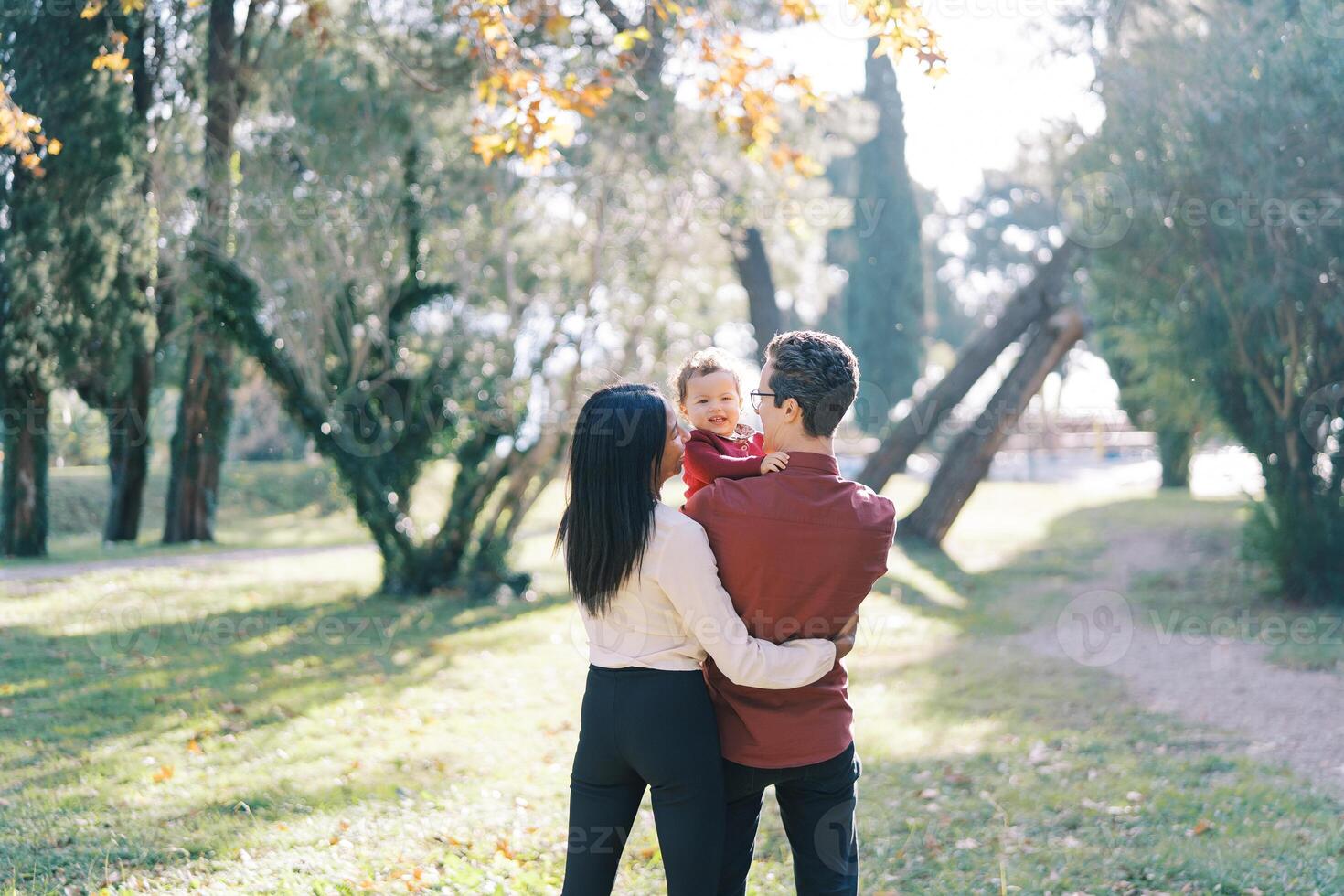 poco ragazza nel il braccia di sua padre, chi è abbracciato di sua madre. indietro Visualizza foto