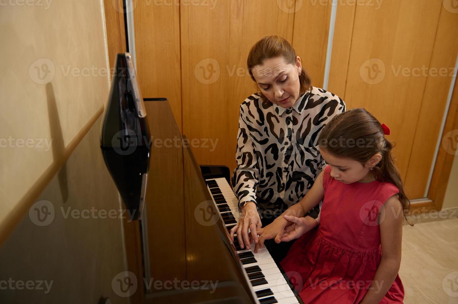 elementare età poco pianista ragazza giochi pianoforte, comporre un' melodia sotto il guida di sua insegnante durante individuale musica lezione a casa. bambini. formazione scolastica. stili di vita. Hobby e divertimento foto