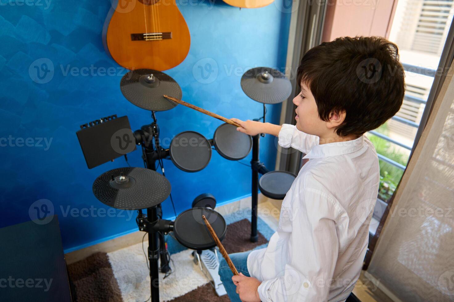 alto Visualizza di un' ispanico adolescente ragazzo musicista utilizzando bacchette, battito su il tamburo mentre l'esecuzione suoni, sensazione il ritmo di musica. tamburo impostato - percussione musicale strumento. foto