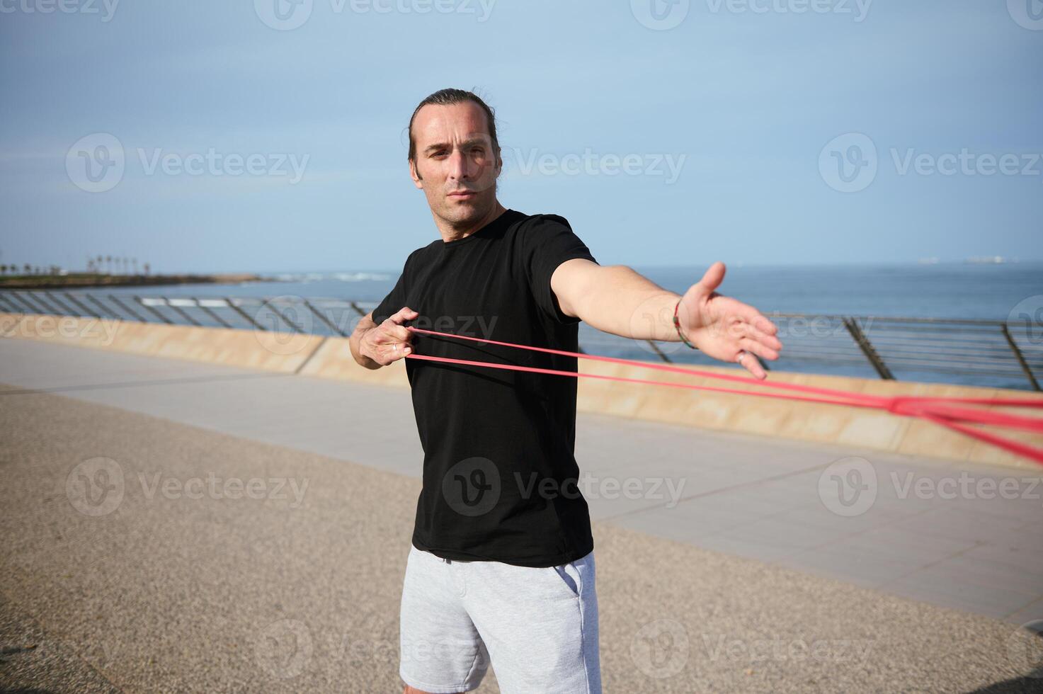 giovane atleta fare braccia, bicipite e spalla esercizi con resistenza fitness gomma da cancellare bande su il spiaggia all'aperto foto