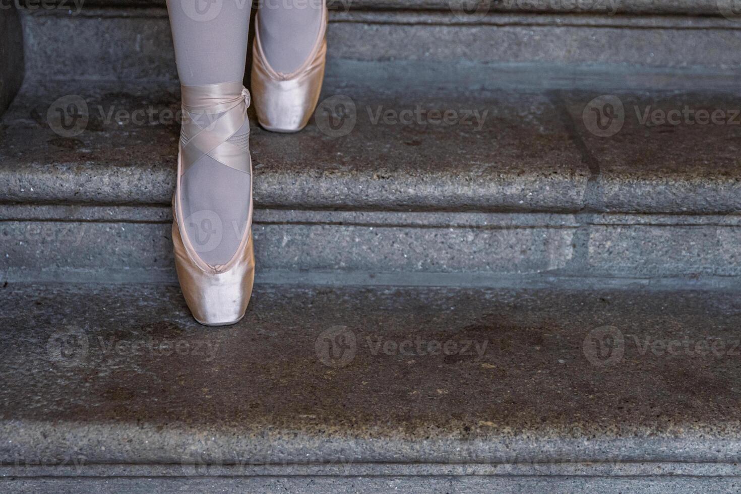 avvicinamento di di ballerina pointes su il grigio pietra passaggi sfondo. danza seduta su il passi. ballerina piedi con rosa balletto pantofole Su. minimalista, semplice. copia spazio. foto