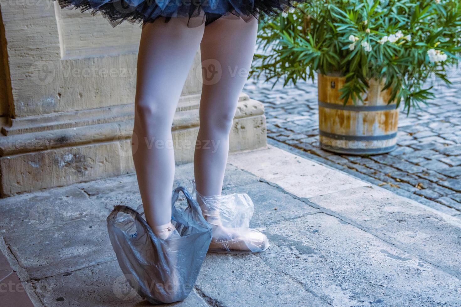 ballerina in piedi su il pietra pavimento indossare pointe scarpe con nero e bianca plastica Borsa proteggere scarpe. balletto ballerino con bianca collant Su. dietro le quinte. strada prestazione. concetto. divertente foto