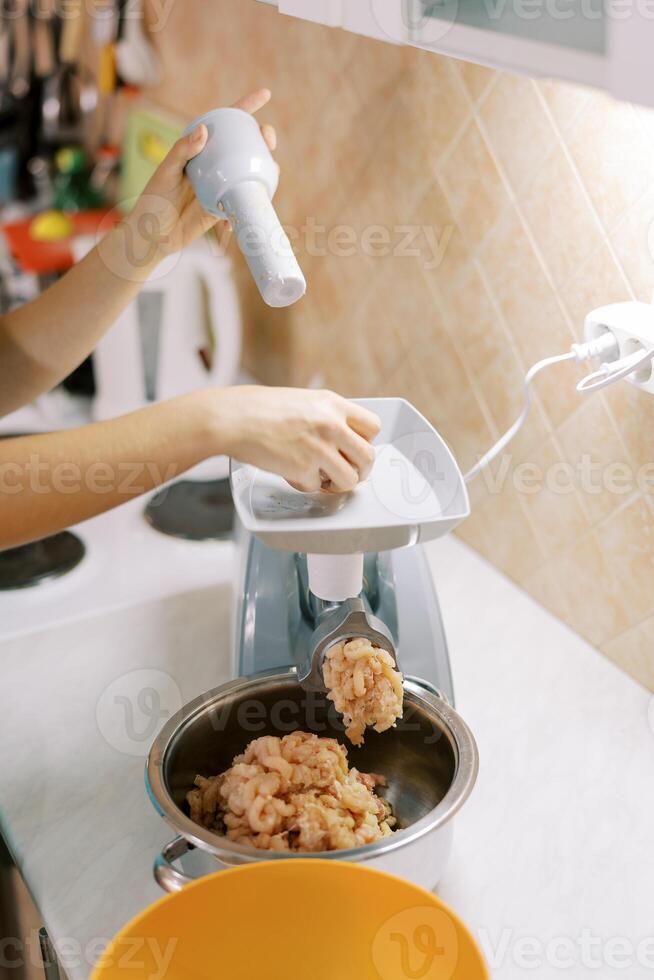 casalinga fa tritato carne su un elettrico carne macinino spingendo il carne nel il vassoio con un' pusher foto
