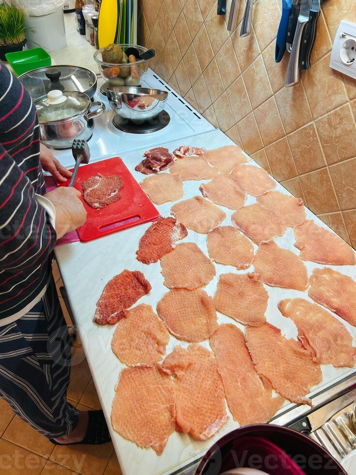 casalinga fa braciole di carne con un' martello su un' taglio tavola su il tavolo foto