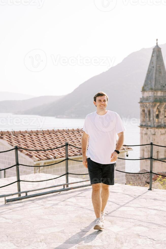 giovane uomo passeggiate lungo il osservazione ponte vicino il campanile di il Chiesa di st. nicola. perasto, montenegro foto