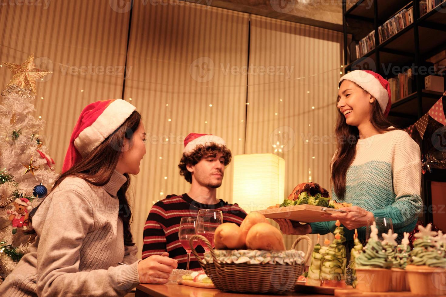 il pasto speciale di una famiglia, la giovane donna serve tacchino arrosto agli amici e allegra con un drink durante una cena nella sala da pranzo di casa decorata per la festa di Natale e la festa di capodanno. foto