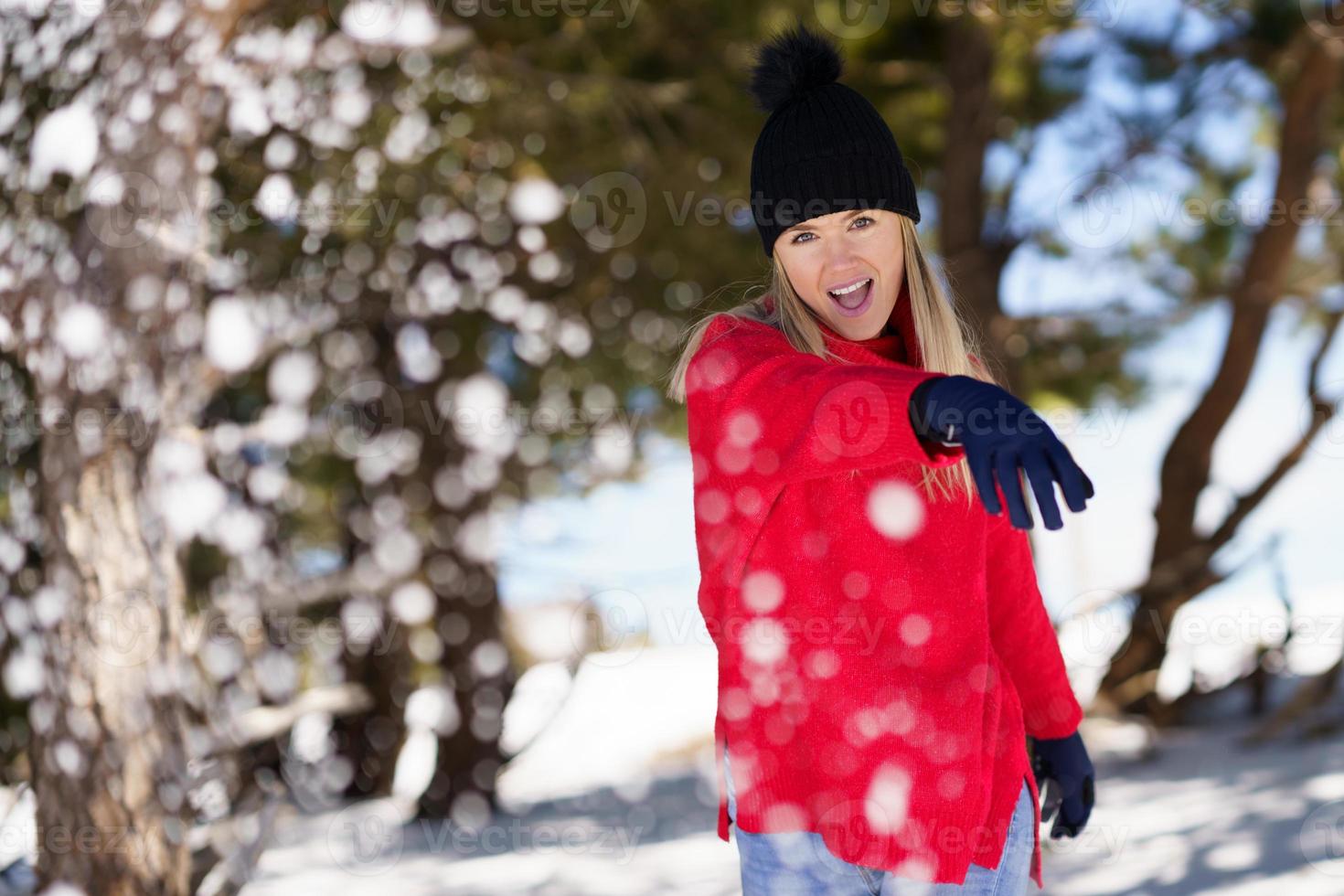 donna bionda che lancia palle di neve in avanti in una foresta innevata in montagna foto