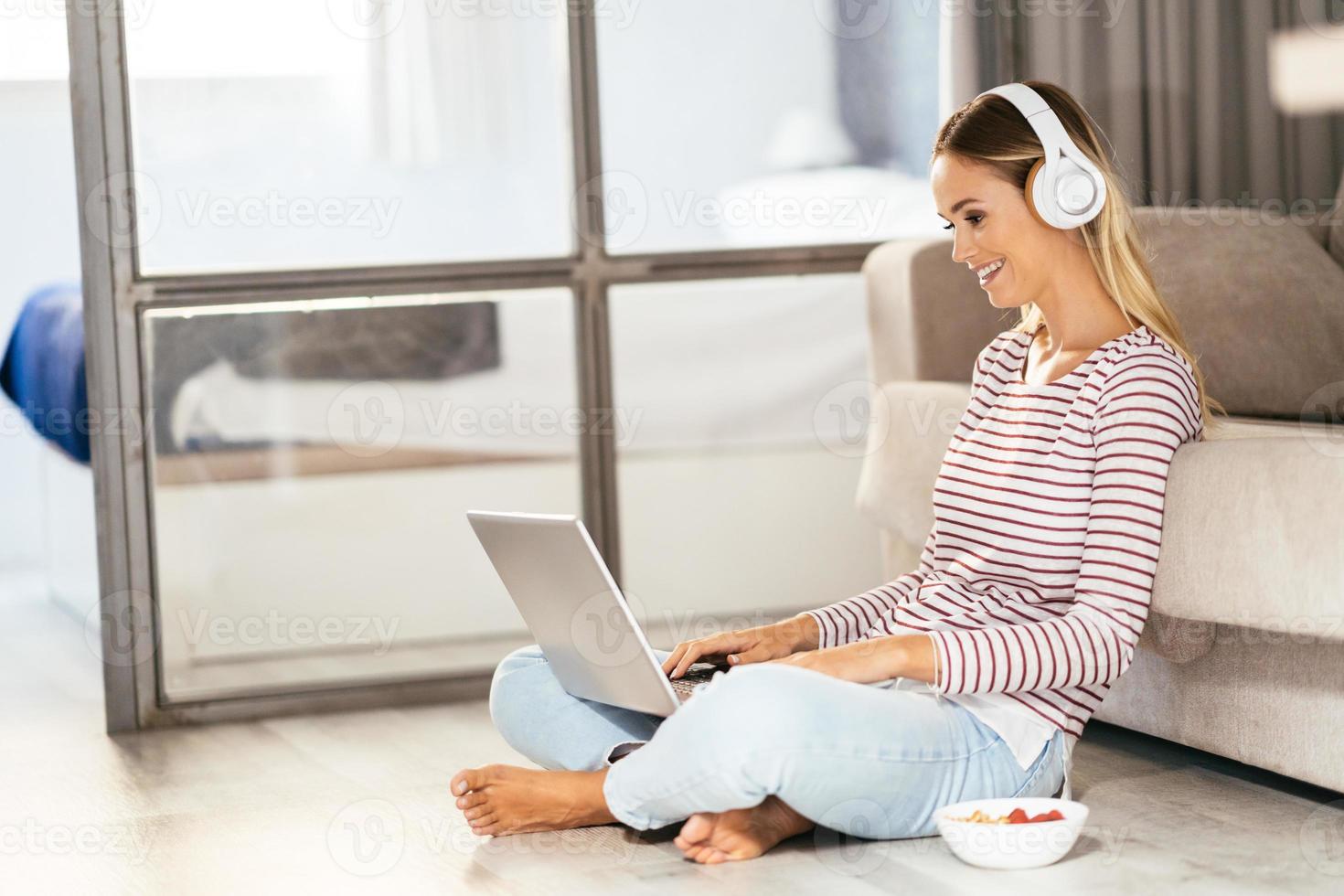 giovane donna sorridente con cuffie e laptop sul divano foto