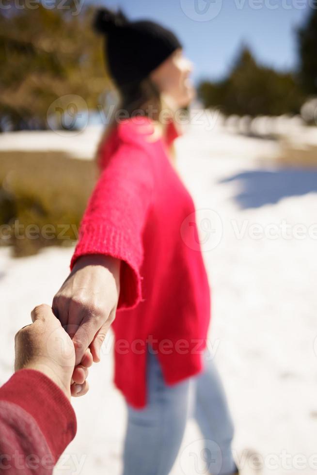 donna bionda in abiti invernali che cammina tenendo la mano del suo partner tra le montagne innevate. foto