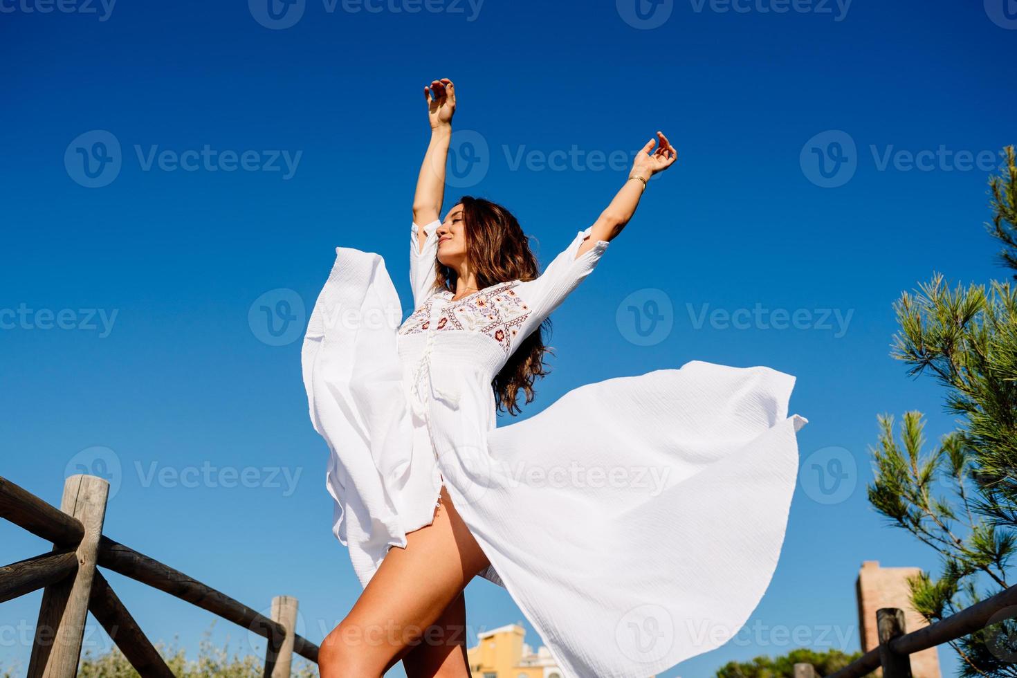 giovane donna che alza le braccia in un bellissimo abito bianco contro un cielo blu foto