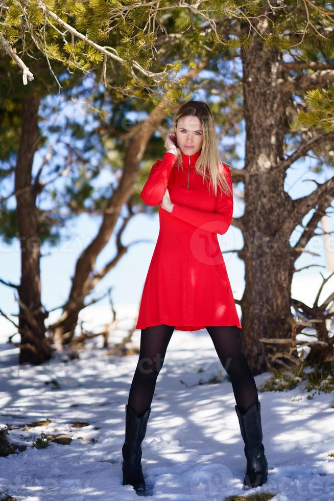 donna bionda che indossa un abito rosso e calze nere nelle montagne innevate in inverno. foto