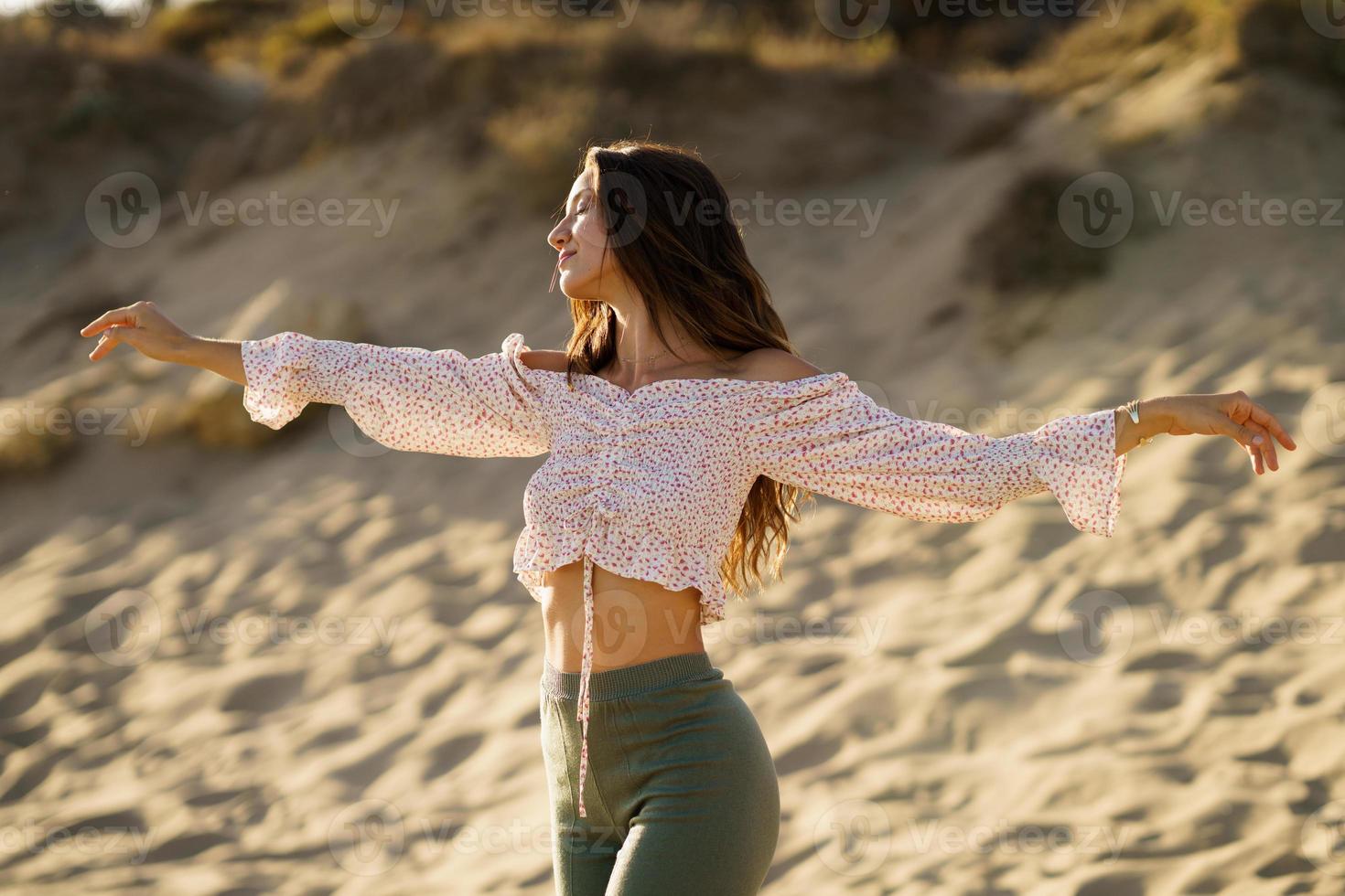 giovane donna alzando le braccia in piedi sulla sabbia della spiaggia foto