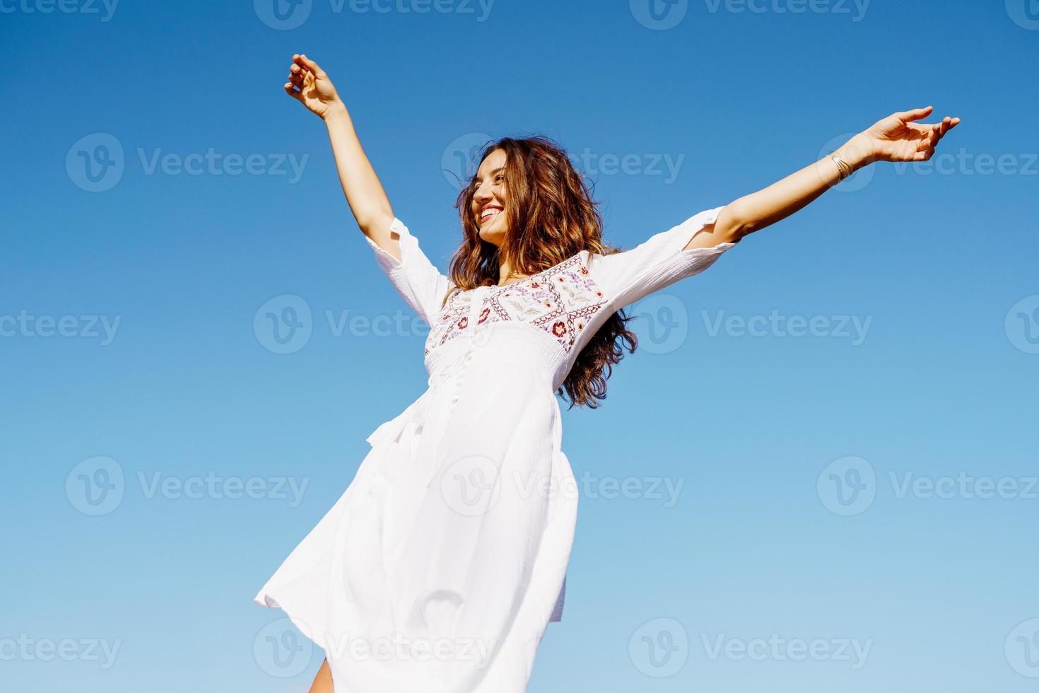 giovane donna che alza le braccia in un bellissimo abito bianco contro un cielo blu foto