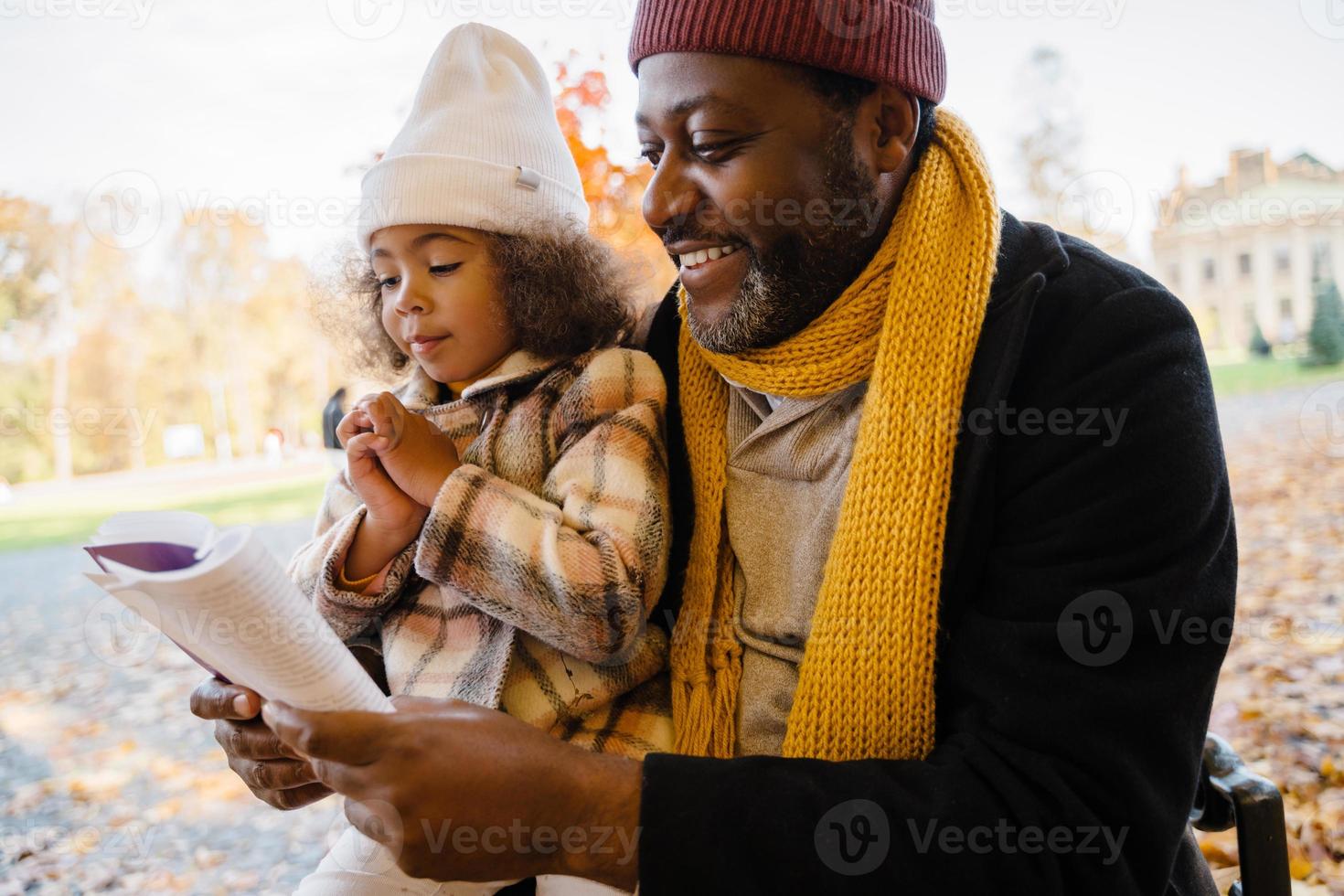 nonno nero e nipote che leggono un libro durante le passeggiate nel parco autunnale foto