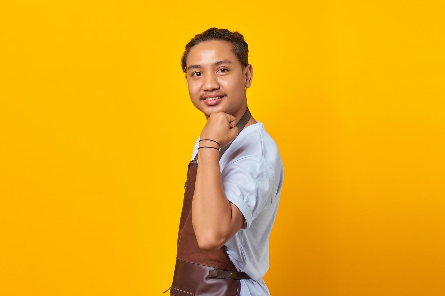 ritratto di un giovane asiatico fiducioso che indossa un grembiule che mostra i muscoli del braccio mentre sorride con orgoglio su sfondo giallo foto