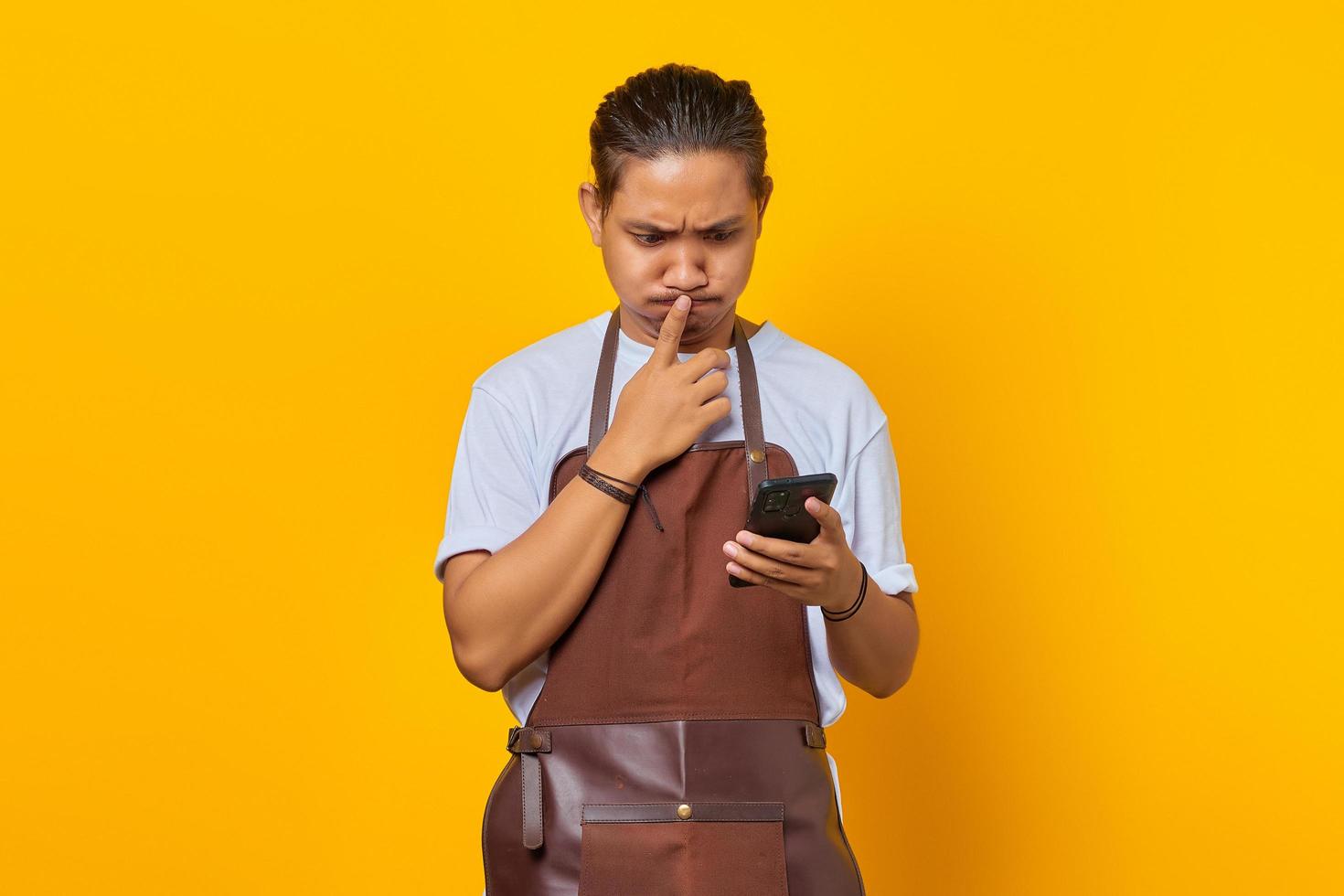 il giovane uomo asiatico che tiene lo smartphone sembra ansioso e preoccupato ha paura di qualcosa di isolato su sfondo giallo foto