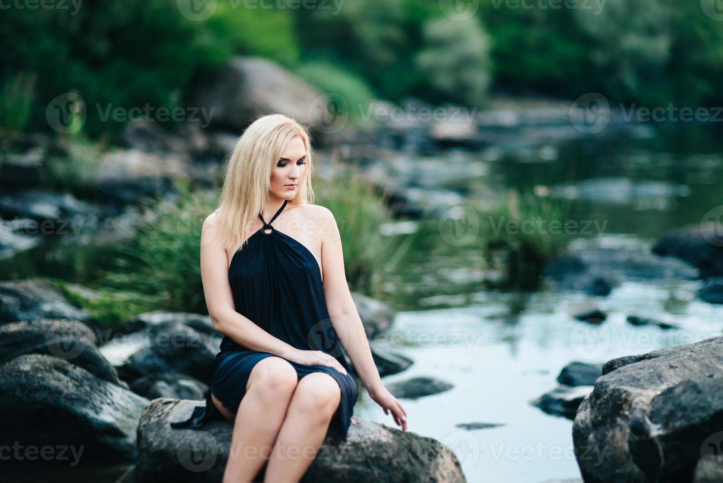 ragazza bionda in un vestito nero con gli occhi azzurri sulla costa del fiume foto