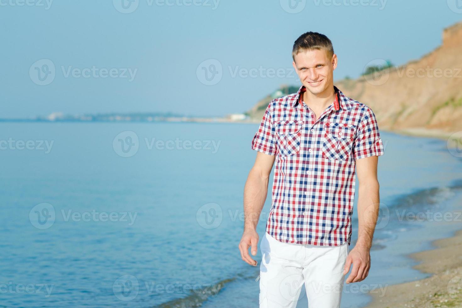 ragazzo in pantaloni bianchi cammina lungo la riva del mare contro foto