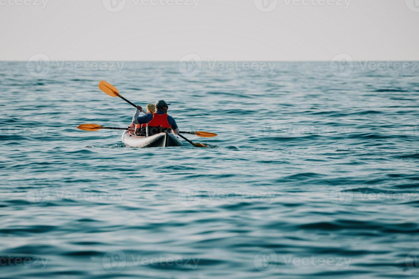 contento coppia kayak nel un gonfiabile kayak su il mare a tramonto. coppia canoa nel il mare vicino il isola con montagne. persone kayak nel vita giacche vela. indietro Visualizza foto