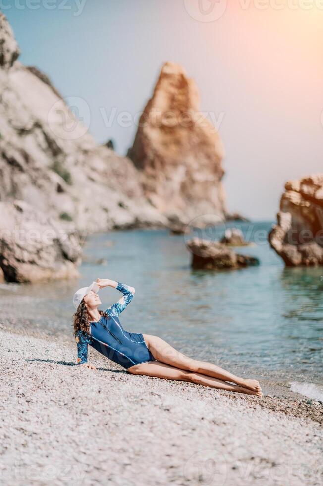 ritratto donna mare. bene guardare mezzo anziano donna con nero capelli, fitness istruttore nel blu costumi da bagno su il roccioso spiaggia vicino il mare. femmina fitness yoga routine concetto. salutare stile di vita. foto