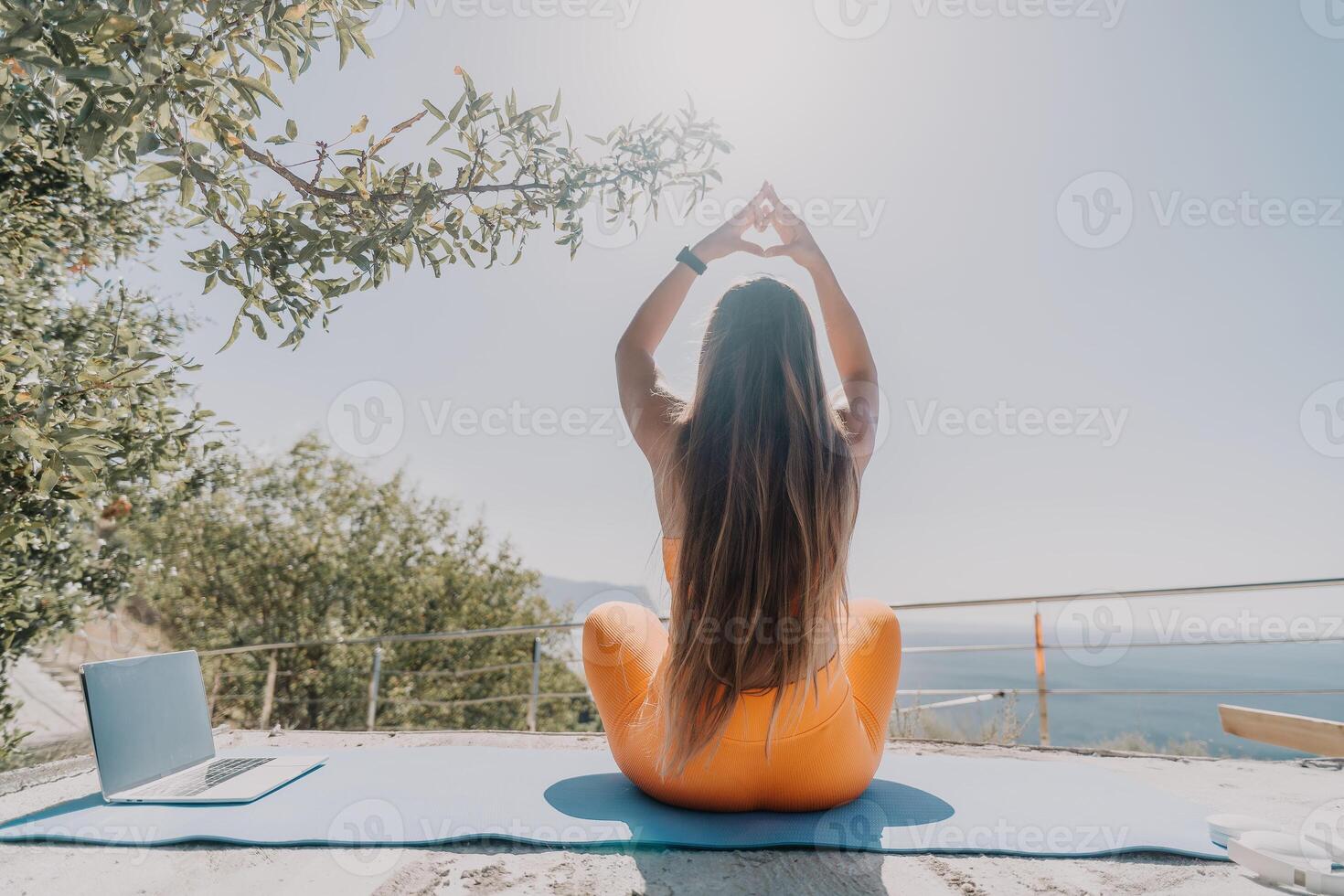 fitness donna mare. contento mezzo anziano donna nel arancia abbigliamento sportivo esercizi mattina all'aperto su yoga stuoia con il computer portatile nel parco al di sopra di oceano spiaggia. femmina fitness pilates yoga routine. salutare stile di vita. foto