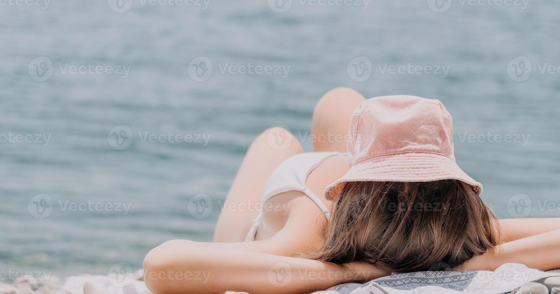 irriconoscibile positivo donna nel bianca bikini prendere il sole o concia su mare spiaggia durante estate. contento turista godendo sole abbronzatura dire bugie su spiaggia sedia sala a lusso ricorrere foto