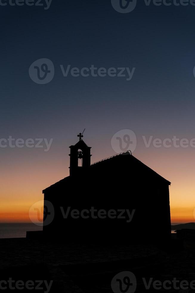 silhouette di un' Chiesa con un' campana Torre su il tetto contro il tramonto cielo foto