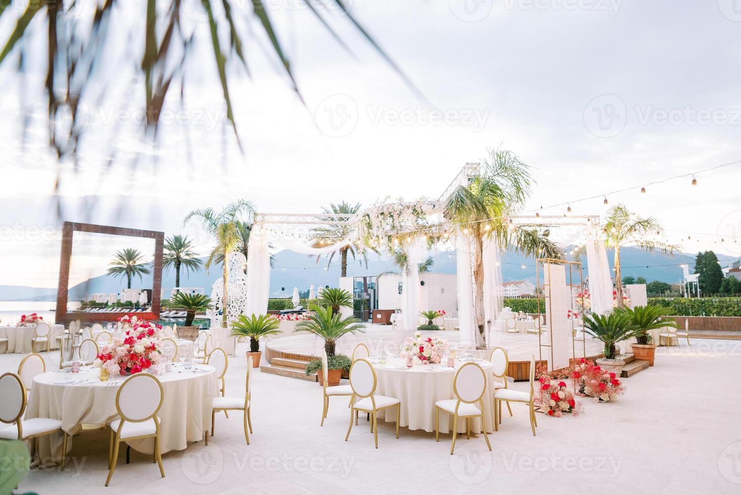 festivo tavoli con colorato mazzi di fiori di fiori In piedi in giro un' il giro palcoscenico su il riva del mare contro il sfondo di montagne foto