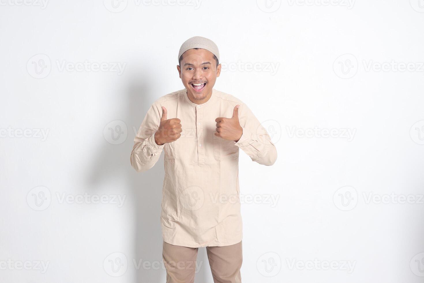 ritratto di attraente asiatico musulmano uomo nel koko camicia mostrando pollice su, bene lavoro mano gesto. approvazione concetto. isolato Immagine su bianca sfondo foto