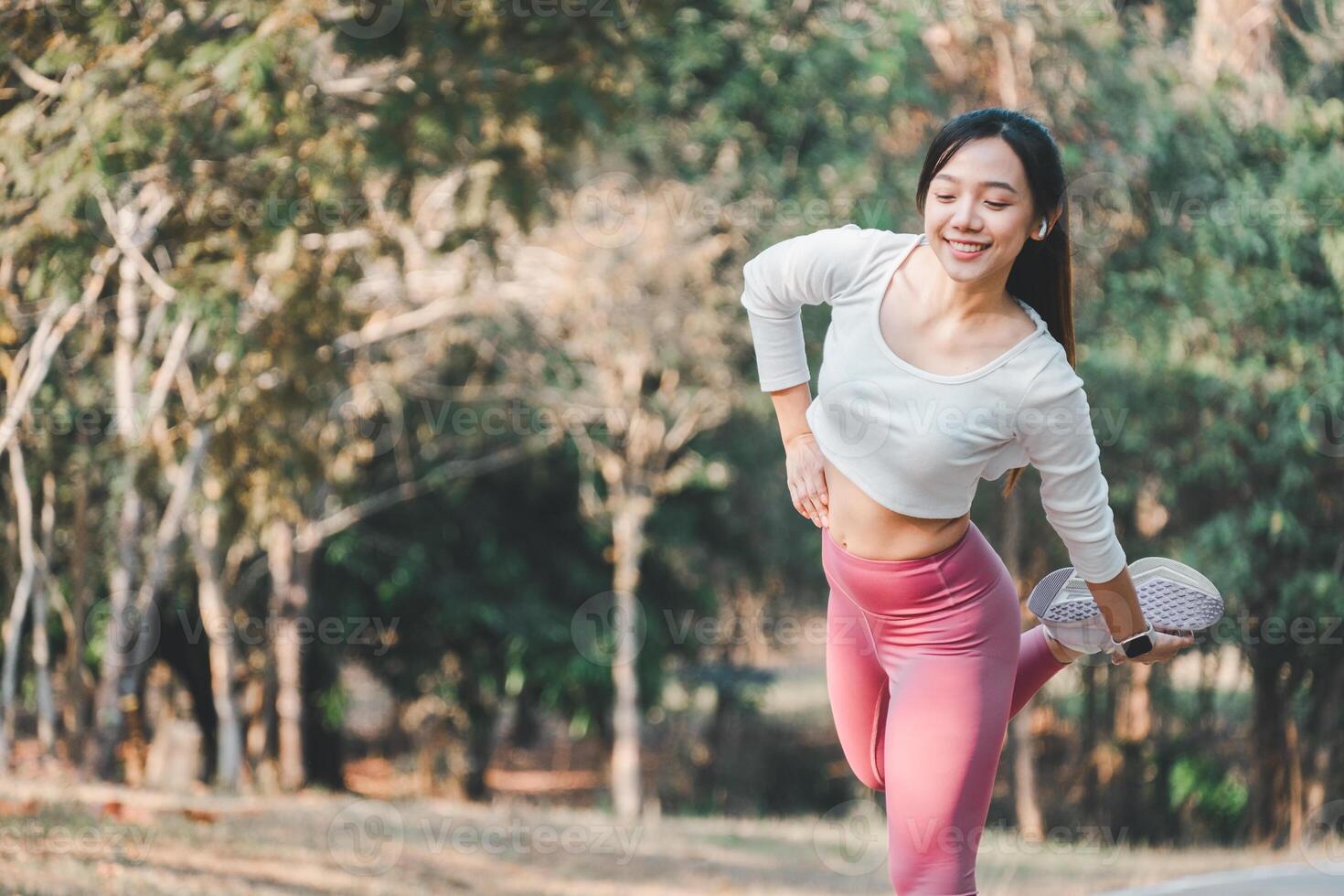 un' sorridente giovane donna esegue un' gamba stirata, equilibratura su uno piede nel un' soleggiato parco, evidenziazione il importanza di flessibilità nel fitness routine. foto