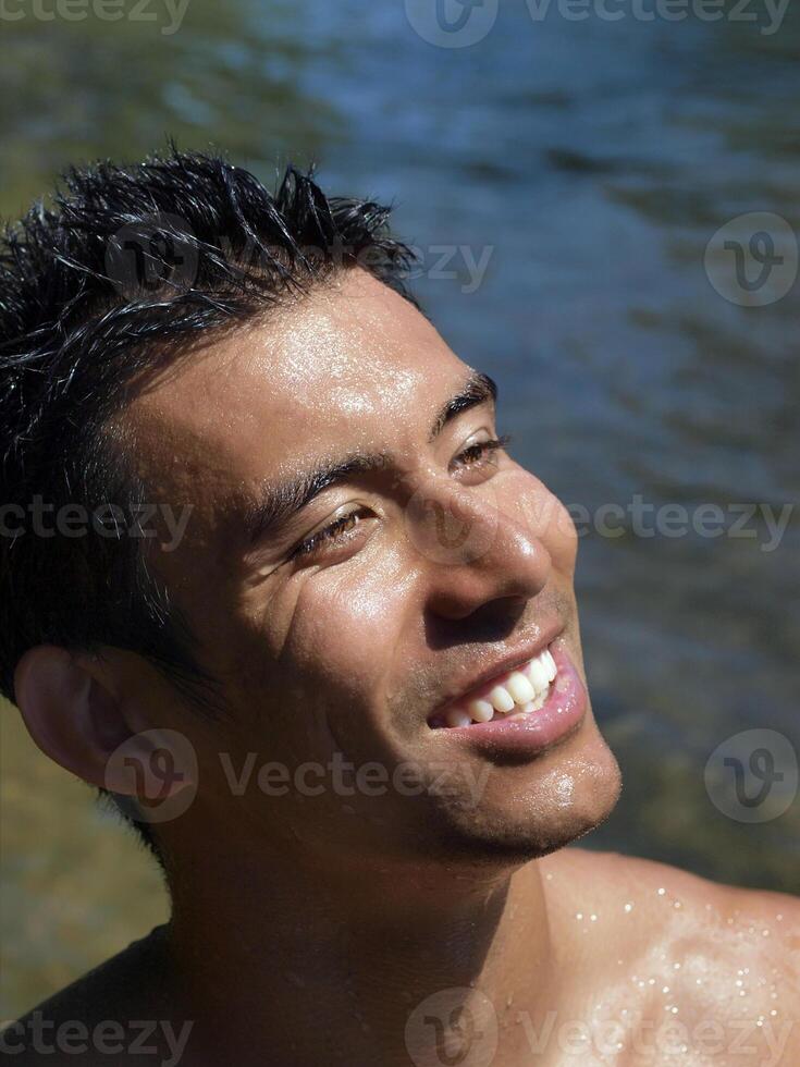 sorridente giovane uomo gocciolante con acqua a fiume foto