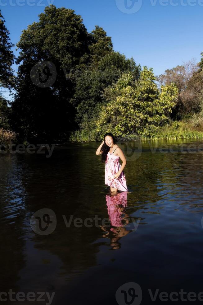 sorridente giovane giapponese americano donna in piedi nel fiume foto