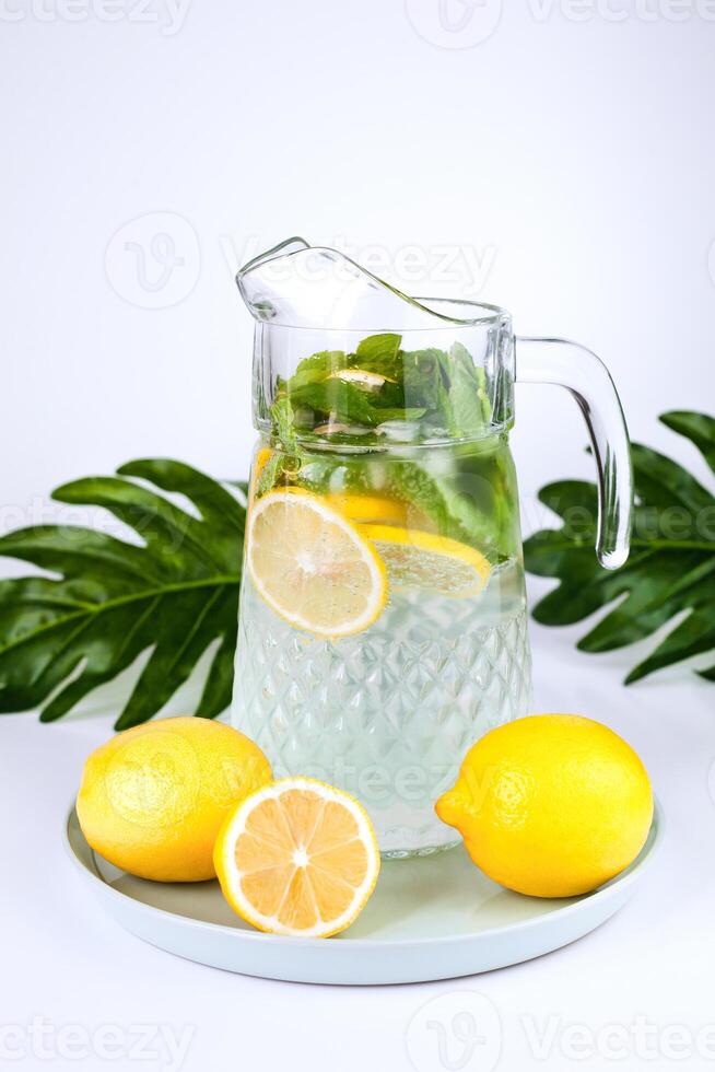 un' brocca di limonata con Limone fette, fresco menta e ghiaccio cubi su il tavolo. fabbricazione fresco limonata. avvicinamento. foto