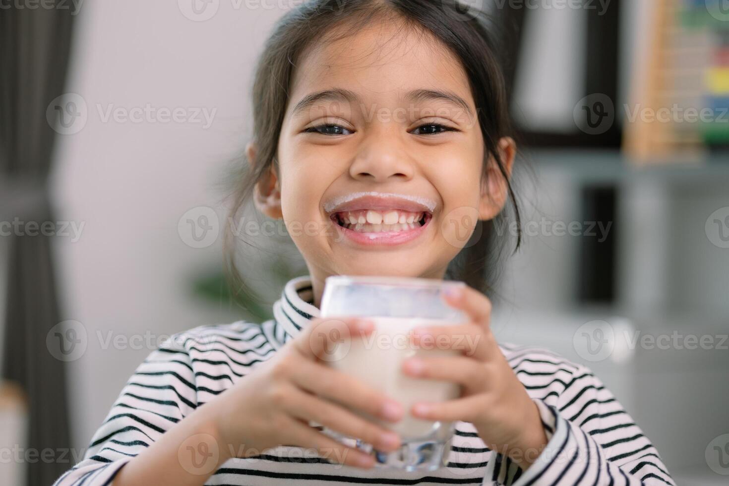 asiatico poco carino ragazza potabile latte giovane prescolastico bambino ragazza o figlia soggiorni casa con un' sorridente viso, si sente felice, e gode potabile latte. foto