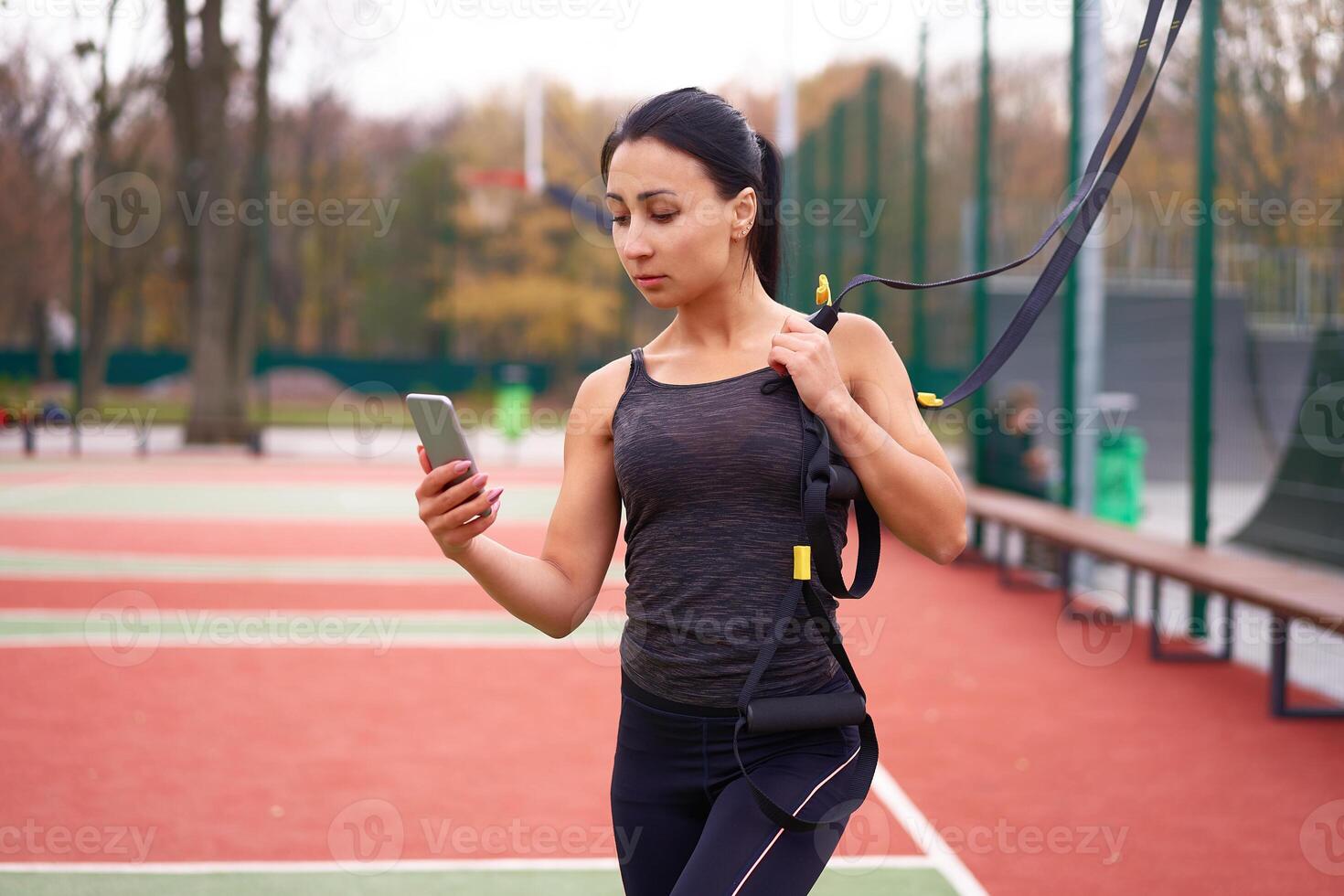 ragazza atleta formazione utilizzando su Campo sportivo. misto gara giovane adulto donna fare allenarsi con sospensione sistema. salutare stile di vita. allungamento all'aperto terreno di gioco. foto